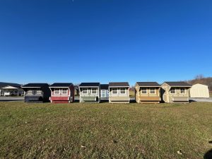 Row of Old Hickory Chicken Coops with nesting boxes and metal roofs on sales lot, durable backyard buildings for farm or ranch use