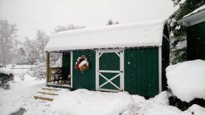 Old Hickory Lofted Barn with Side Porch and single barn door, outdoor storage building in snowy winter residential backyard