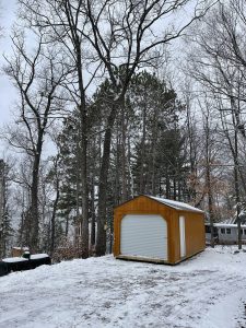 Old Hickory Utility Shed with Garage package, roll-up door and solid house door in snowy wooded backyard