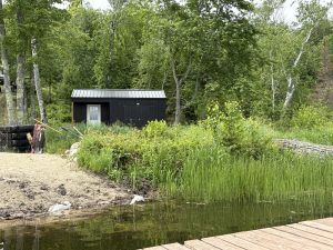 Old Hickory Utility Shed with Side Porch package in Tricorn Black with black metal roof, wooded lakeside setting