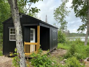 Old Hickory Utility Shed with Side Porch package, railing and double barn doors, outdoor storage shed in wooded lakeside landscape