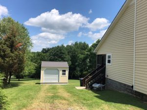 Old Hickory Utility Shed with Garage package, roll-up door and white trim, outdoor storage shed in tree-filled backyard