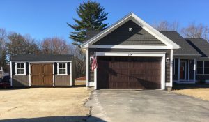 Old Hickory Side Utility outdoor storage shed with shingle roof and window shutters beside home garage