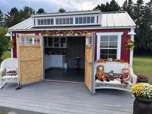 Old Hickory Utility Shed with dormer, porch deck and open double barn doors revealing interior counter space, stylish backyard storage shed