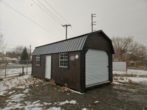 Old Hickory Side Lofted Barn with garage roll-up door, windows and metal roof, portable storage building on snowy winter sales lot