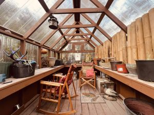 Old Hickory Greenhouse interior with clear roof panels, backyard greenhouse transformed to cozy garden studio with gardening pots and rocking chairs