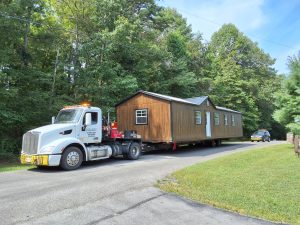 Old Hickory Utility Shed with gable dormer and metal roof being delivered by trailer to residential property